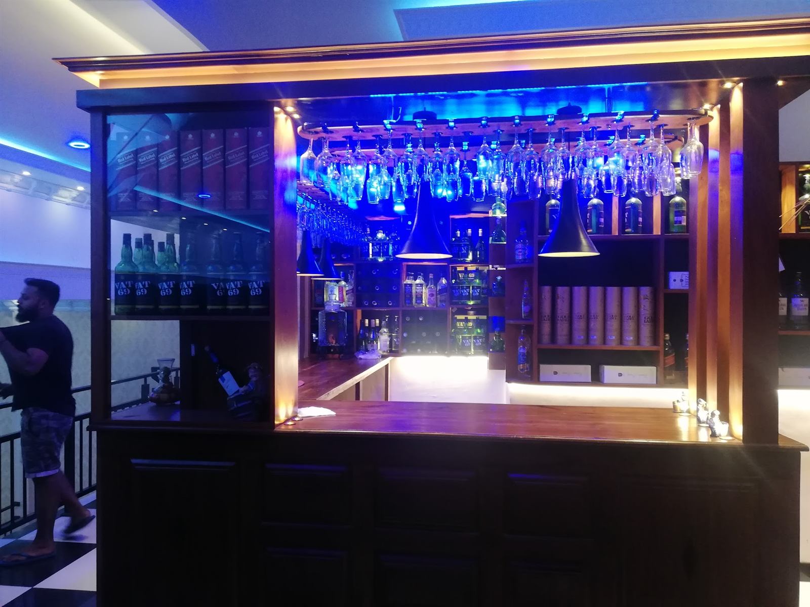 The wooden bar counter, lit blue, with rows of glasses hanging above it